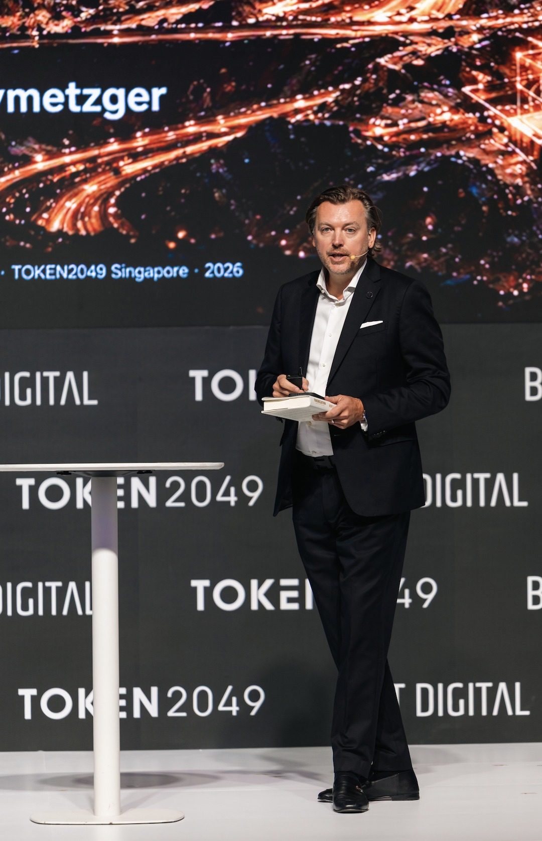 Monty Metzger holding his book Tokenization: Capital for Humanity while speaking at TOKEN2049 Singapore 2026