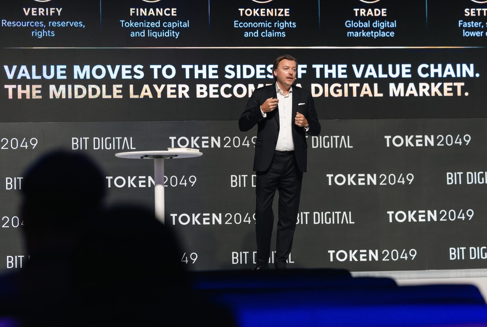 Monty Metzger, speaker at TOKEN2049 Singapore 2026, on stage with the slide Value moves to the sides of the value chain, the middle layer becomes a digital market