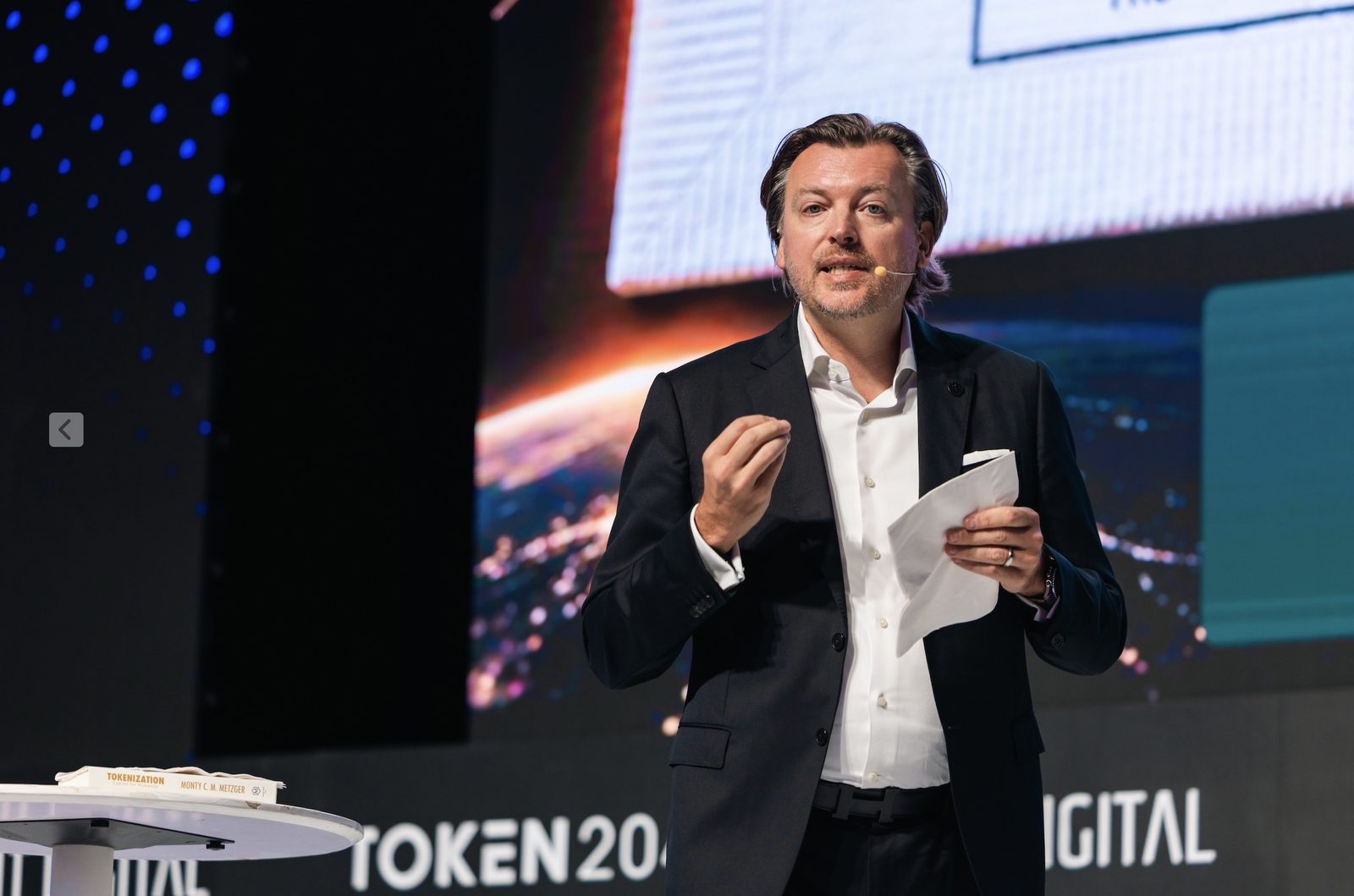 Close-up of Monty Metzger speaking at TOKEN2049 Singapore 2026 with his book Tokenization: Capital for Humanity on the lectern
