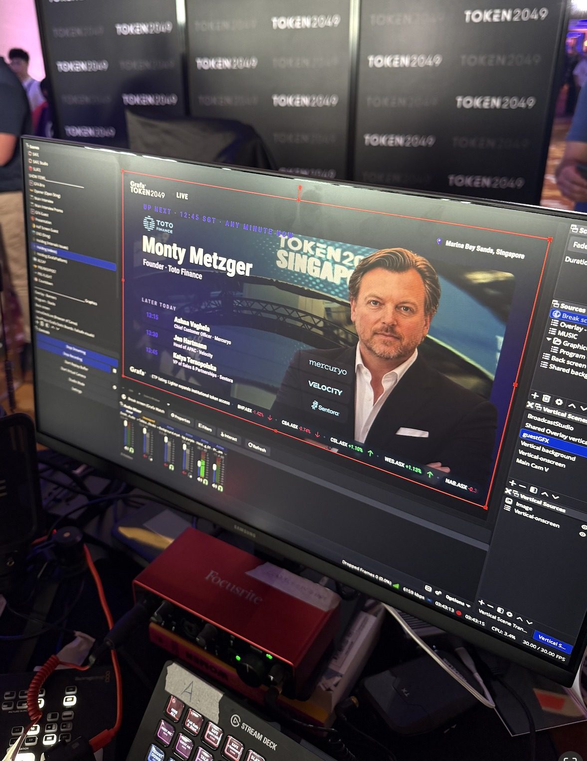 Broadcast monitor showing Monty Metzger, Founder of Toto Finance, up next in the live TOKEN2049 Singapore interview program at Marina Bay Sands